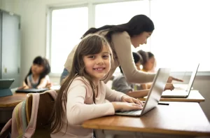 A young girl smiling at the camera while sitting in front of a computer